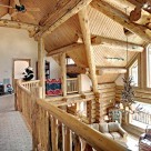 View from loft of luxury log home looking into greatroom over log raings. Exposed log valley, log posts and purlins create dramatic ceiling and massive antler chandelier hangs in front of stone fireplace.
