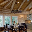 Large round wodden dining table with beautiful caned chairs in dining room of luxury log home with wide plank wood floors, whitewash log ceiling beams and custom metal chandelier.