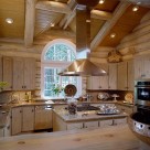 Large copper range hood suspended from log beams in kitchen of luxury log home with custom cabinetry granite counters and wide plank log breakfast bar.