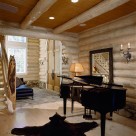 Inteior of custom log home with wide plank wood floors, baby grand piano in fore ground and massive arched entry doors in background. Log newel post with custom carve indian