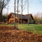 Exterior of handcrafted log home set in Pennsylvania forest. Log home has stone wall in front and large doors and windows to side.