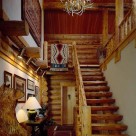Log staircase with log rails leading to loft inside handcrafted log home. Bear carving in foreground and antler chandelier hanging above.