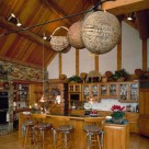 Interior kitchen with wood floors, one stone wall and cathedral ceilings with log purlins and pine ceiling. Pine cabinetry with glass doors behind breakfast bar with bar stools.