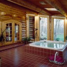 Jacuzzi spa set on red tile in enclosed porch of luxury log home with round top french doors leading into home and out to Pennsylvania forest