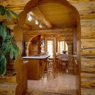 Kitchen and dining room with slate floors viewed through log archway in custom log home. Breakfast bar with barstools.