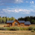 Luxury log home with metal roof set in meadow with Colorado forest behind.