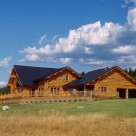 Exterior of custom log home with attached garge and large front deck lined with log railings.