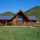 Exterior of ranch style handcrafted log home set in Colorado meadow with mountains behind.