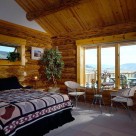 Master bedroom in handcrafted log home with wicker chairs set next to large windows looking out to Colorado mountains.