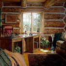 Office with oak table and high back red leather office chair in log home built with massive handpeeled logs with white chinking material between logs.