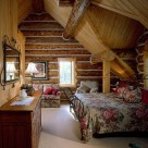 Loft bedroom with iron bedframe set in dormer of handcrafted log home.