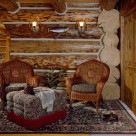 Sitting area with wicker chars and ottoman on area rug set against log wall with massive logs.