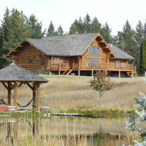 Exterior of log home viewed across pond with log gazebo