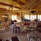Interior great room of handcrafted log home with cathedral ceilings with log truss and log purlins above large white sectional couch on carpeting.