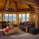 Colorado rocky mountains viewed through large pine trimmed windows in sunroom of handcrafted log home with log archway and exposed log rafters and knotty pine ceiling.s