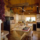 Log home kitchen with light brown tile floors, custom pine cabinets and island. Unique log lighting frame suspended by chains from cathedral ceiling.