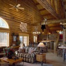 Extrodinary log home greatroom with soaring ceilings and massive log trusses. Fabric love seat sits on Navajoe area rug and mountain lion mount is perched on log beam above with antler chandelier lighting the space.