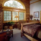 Master bedroom in handcrafted log home with cozy chairs large Armoire and twelve foot wide window with radius top showing view of Colorado forest.