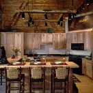 Custom kitchen with wood cabinetry and large breakfast bar with lovely bar stools in handcrafted log home. Unique log frame with spot lights attached is suspended by chains
