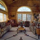 Handcrafted log home living room with massive french doors and semicircle windows above. Soaring cathedral ceiling above large sofa's set on indian style area rug.
