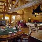 Amazing game room in custom log home with poker table and log framed cuatom pool table. Enormous log truss and log beams support cathedral roof above and blackbear rug is mounted on log wall.