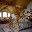 Custom log bed with handcarved fish inlaid into headboard in loft bedroom with gable dormer and exposed log purlins with pine ceiling boards.