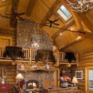 Bear rugs draped over log railings above massive river rock fireplace in full scribe log home with timber frame truss and antler chandelier.