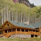 Luxury log home with wrap around porches, bay window with copper trim and river rock patio set in aspen forest below red rock cliffs.