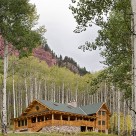 Luxury log home with wrap around porches, three story bay window with copper trim and river rock patio set in aspen forest below red rock cliffs.