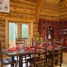 Dining room table and chairs in handcrafted log home with views through french doors to forest. Custom red china hutch in corner.