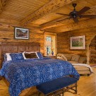 Luxurious bedroom in handcrafted log home with sitting area through log archway. Shiny hardwood floors, king size bed with ceiling fan above.