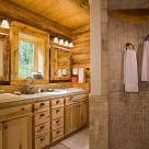Walk in stone shower in handcrafted log home bathroom with custom cabinetry and pine window trim.