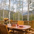 Log table and log chairs set on large deck with log railings with aspen trees in the background.