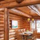 Photo of handcrafted log home dining room with handmade dining table, log post and log beams supporting ceiling with pine T&G boards.