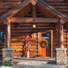 Cloe up photo of log home entry with stone pillars supporting log post and beam with Christmas wreath on door.