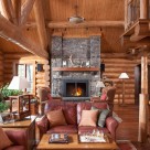 Photo of handcrafted log home great room with Chief Cliff stone fireplace, red leather chairs and cathedral ceilings with log truss.