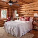 Handcrafted log home bedroom with wood floors, area rug and cozy bed.