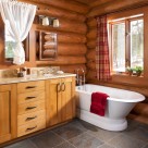 Custom log home bathroom with slate floors, white antique tub, alder cabinets and sconce lighting.