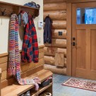 Log home mudroom with Alder door, slate floor, wood bench and coat rack with colorful scarves.