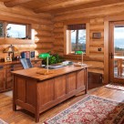 Log home office space with Oak desk, green lamps, wood floors and views through window to Flathead Lake, Montana.