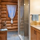 Log home bathroom with slate floors, glass shower and eclectic window treatment.