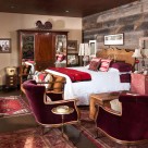 Red velvet chairs in bedroom with reclaimed wood on walls, antique rugs and furnishings.
