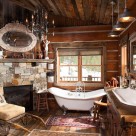 Clawfoot tub next to stone and wood fireplace in bathroom of handcrafted dovetail log cabin.