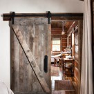 Sliding barnwood door with black metal hardware in chink style log cabin.