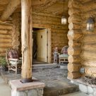 Photo of Scandinavian full scribe log home entry porch with stone patio and wicker chairs.