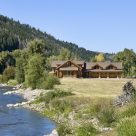 Photo of Massive log home on Yampa river in Colorado with three car attached garage, multiple roof lines and green field in foreground.