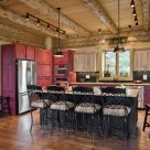 Photo of log home kitchen with hardwood floors, red cabinets, exposed log beams with pine ceiling.