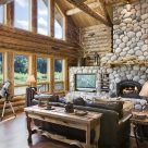Handcrafted log home great room with river rock fireplace and large windows with views to river and forest beyond.