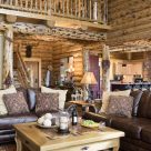 Log home living room with leather sofas, custom coffee table and character log posts supporting log catwalk with log railings.