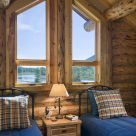 Close up photo of log home bedroom with twin beds, rustic nightstand and trapezoid windows in log gable.